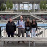 three young women and man in bowtie pose for photo on UAlbany campus