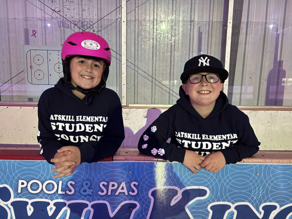 two students smiling and wearing helmets on ice rinks