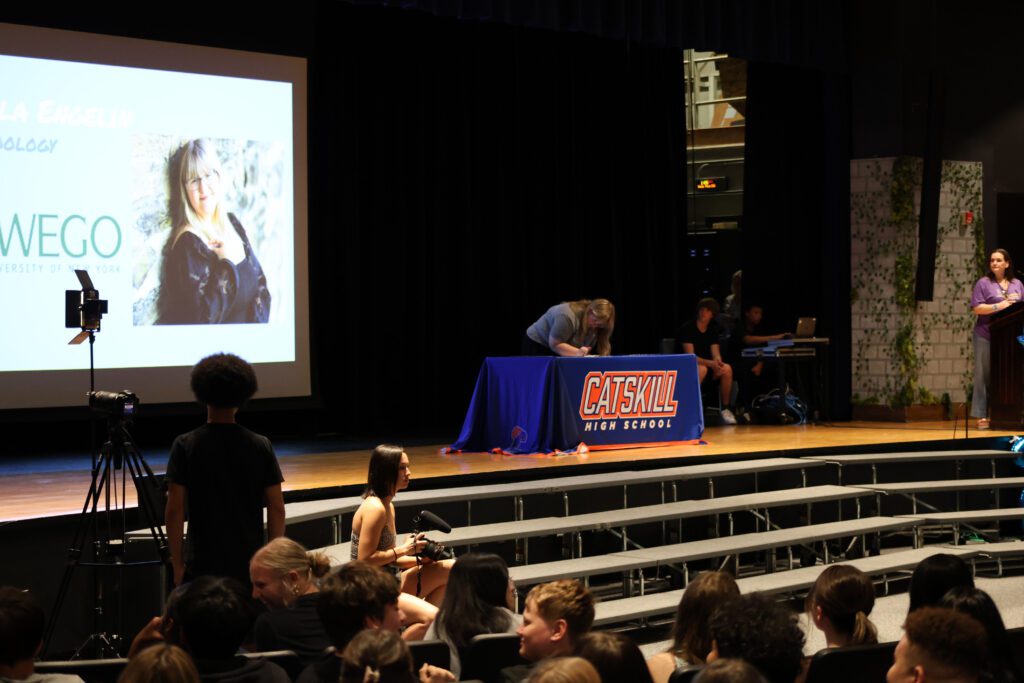 student signing letter at table on stage
