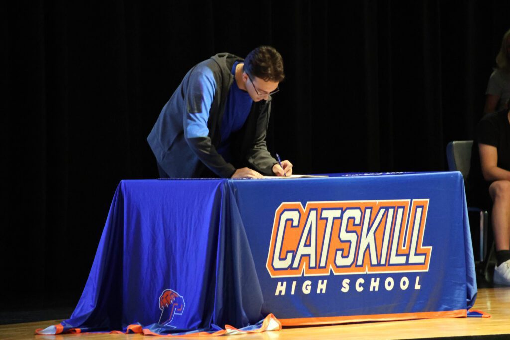 student signing letter at table on stage