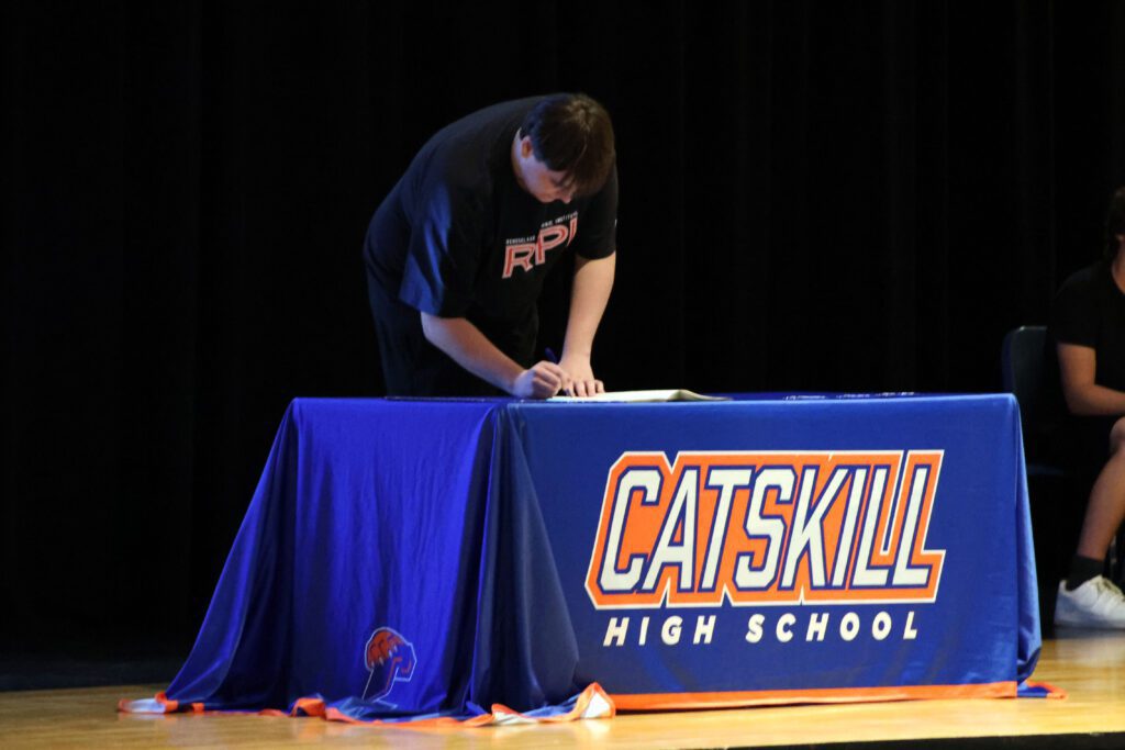 student signing letter at table on stage